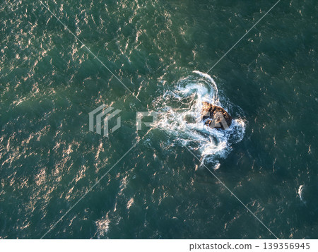 Waves swirl around a rock in the ocean during daylight hours Waves swirl around a rock in the ocean during daylight hours 139356945