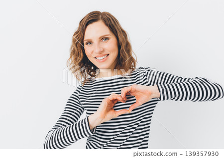 Woman in striped shirt makes heart gesture while smiling warmly 139357930