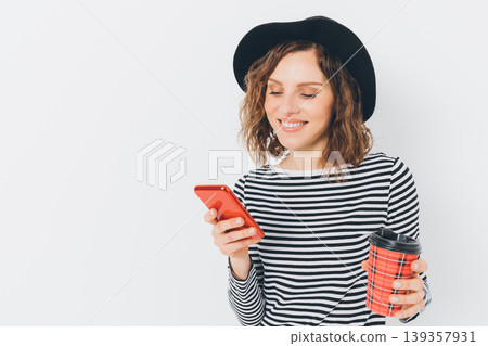 Woman with curly hair holding phone and takeaway cup Woman with curly hair holding phone and takeaway cup 139357931