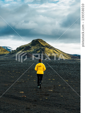 Female hiker exploring with moss covered volcanic mountain on black sand terrain in Iceland 139358010