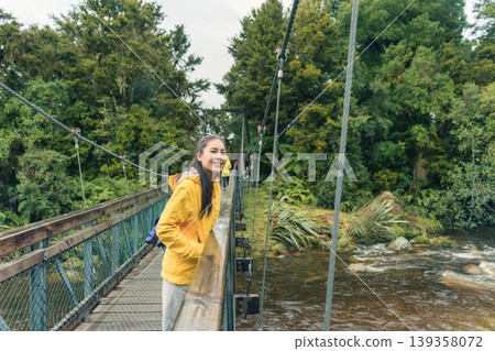 Asian woman smiling on suspension bridge in lush forest at Lake Matheson, New Zealand 139358072