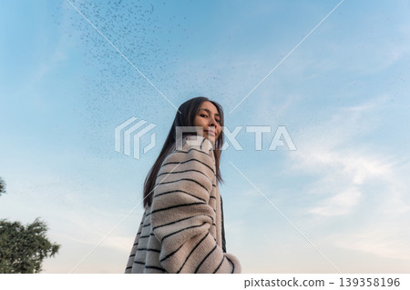 Asian woman smiling and enjoying with flock of bats flying in blue sky during the evening Asian woman smiling and enjoying with flock of bats flying in blue sky during the evening 139358196