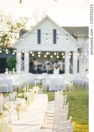 Elegant wedding long table with candle, white rose flower and white chairs in the garden Elegant wedding long table with candle, white rose flower and white chairs in the garden 139358223