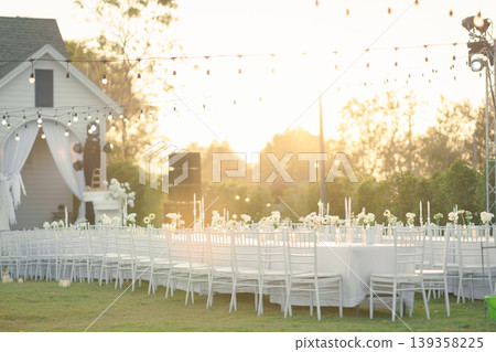 Elegant wedding long table with candle, white rose flower and white chairs in the garden 139358225
