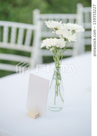 Elegant wedding long table with blank sign, white rose flower and white chairs in the garden 139358227