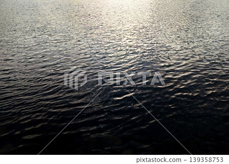 The abstract background features a striking contrast between the shimmering ripples on the water's surface in the setting sun and the deep, ethereal light. The abstract background features a striking contrast between the shimmering ripples on the water's surface in the setting sun and the deep, ethereal light. 139358753