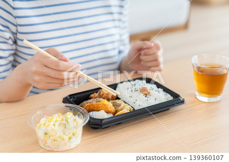 一位年輕女子正在吃便利商店的便當盒,她的手在吃。 一位年輕女子正在吃便利商店的便當盒,她的手在吃。 139360107