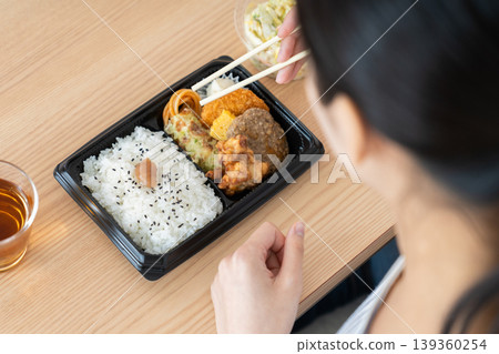 A young woman's hands as she eats a convenience store bento box. 139360254