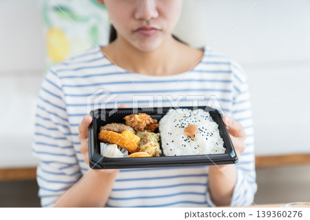 A young woman's hands as she eats a convenience store bento box. 139360276