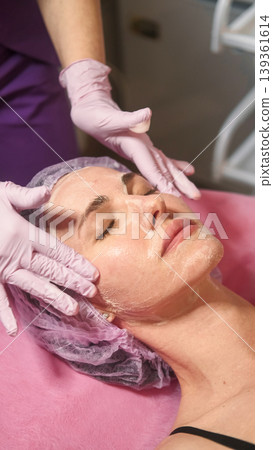 Facial care. Beauty treatment. Professional cosmetologist hands cleansing woman skin on table for skincare procedure in spa salon. Facial care. Beauty treatment. Professional cosmetologist hands cleansing woman skin on table for skincare procedure in spa salon. 139361614