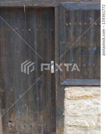 Old dark wooden door with a silver metal handle on a rustic stone building. Old dark wooden door with a silver metal handle on a rustic stone building. 139361772