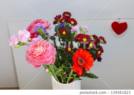 Bouquet of colorful flowers in a white vase with a red heart decoration, creating a bright Mothers Day composition. Bouquet of colorful flowers in a white vase with a red heart decoration, creating a bright Mothers Day composition. 139361821