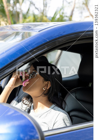A teenager is driving a blue car and is using a pink phone A teenager is driving a blue car and is using a pink phone 139362321