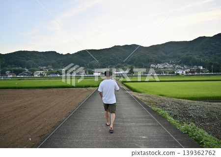 一個男人沿著鄉村公路行走,背景是廣闊的牧場;這是他回家過暑假的景象。 一個男人沿著鄉村公路行走,背景是廣闊的牧場;這是他回家過暑假的景象。 139362762