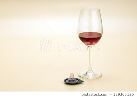Elegant Red Wine Glass Beside an Unwrapped Open Condom on Soft Beige Background, Representing Safe Sex, Responsible Intimacy, and Adult Lifestyle Choices 139363180