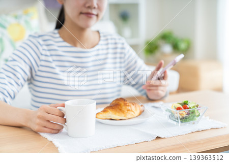 A young woman looking at her smartphone during breakfast 139363512
