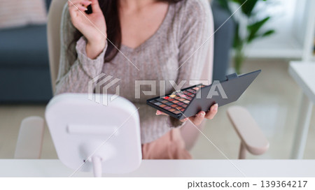 young Asian women holding makeup eyeshadow palette cosmetic product choosing color applying beauty routine sitting home interior living room table mirror soft young Asian women holding makeup eyeshadow palette cosmetic product choosing color applying beauty routine sitting home interior living room table mirror soft 139364217