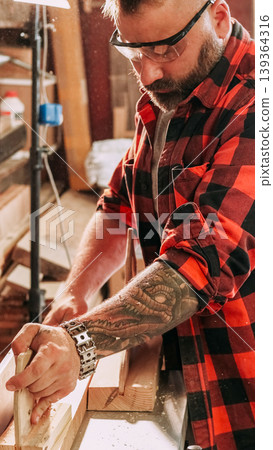 Carpentry workflow. Jointer machine. Male worker with safety glasses smoothing fresh cut plank on professional electric equipment. Carpentry workflow. Jointer machine. Male worker with safety glasses smoothing fresh cut plank on professional electric equipment. 139364316