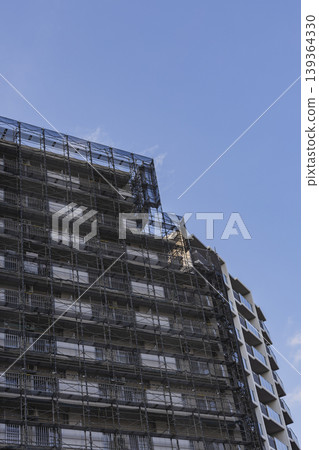 高層建築被鷹架和防護網覆蓋;公寓大樓正在建設中;外牆施工。 高層建築被鷹架和防護網覆蓋;公寓大樓正在建設中;外牆施工。 139364330