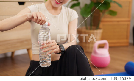 Asian women opening water bottle after home workout exercise session sitting floor with kettlebell fitness equipment healthy lifestyle wellness hydration Asian women opening water bottle after home workout exercise session sitting floor with kettlebell fitness equipment healthy lifestyle wellness hydration 139365379