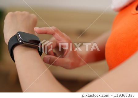 woman using smart watch checking fitness tracker health app wearable technology on wrist active sportswear workout exercise tracking at home lifestyle wellness 139365383