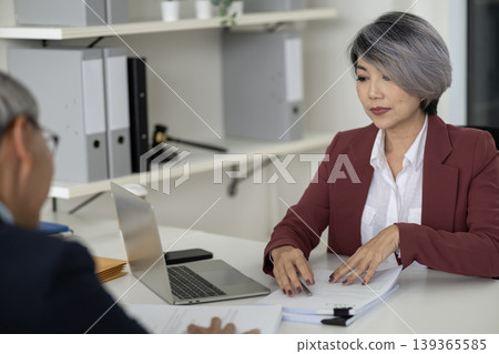 Adult Asian business professional women review financial legal documents collaborate client discuss strategy corporate office setting for important consultation and expert advice 139365585