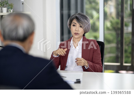 Adult Asian business woman actively explains strategy to colleague in modern office professional discussion meeting workplace environment Adult Asian business woman actively explains strategy to colleague in modern office professional discussion meeting workplace environment 139365588