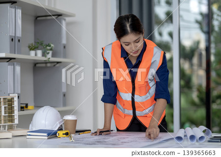 Asian adult woman engineer construction manager project planner reviewing blueprints architectural design documents office site project development Asian adult woman engineer construction manager project planner reviewing blueprints architectural design documents office site project development 139365663