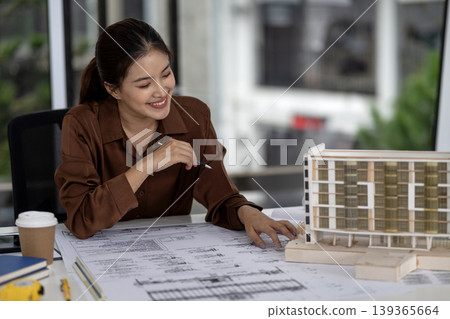 Asian adult woman architect working office reviewing blueprint plans examining building model project design development engineering construction planning happy successful professional career Asian adult woman architect working office reviewing blueprint plans examining building model project design development engineering construction planning happy successful professional career 139365664