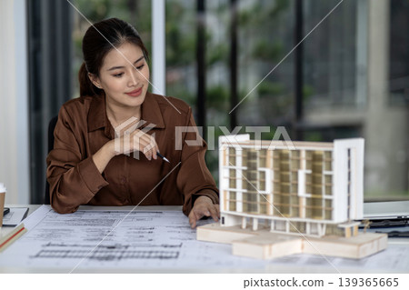 Asian adult woman architect designer reviewing building model plans developing urban design project focused professional work architectural studio 139365665