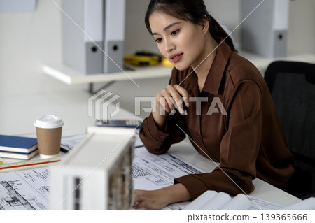 Asian architect woman designs blueprints urban planning engineering office space project development focused professional workspace architectural model Asian architect woman designs blueprints urban planning engineering office space project development focused professional workspace architectural model 139365666
