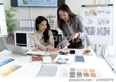 Asian adult women interior designers project planning selecting material samples color palettes modern office workspace design studio 139365679