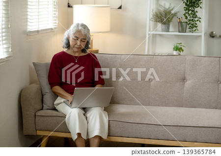 Asian older woman using laptop computer at home sofa learning online focused senior adult browsing internet working remotely from living room Asian older woman using laptop computer at home sofa learning online focused senior adult browsing internet working remotely from living room 139365784