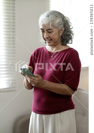 Asian older woman happily uses smartphone at home enjoying digital connection messaging browsing social media online communication lifestyle technology Asian older woman happily uses smartphone at home enjoying digital connection messaging browsing social media online communication lifestyle technology 139365811