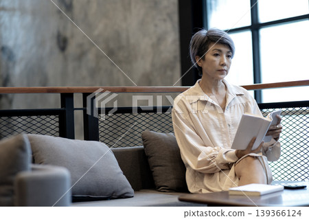 Adult Asian woman relaxing reading book in modern contemporary lounge cafe interior for thoughtful quiet moment Adult Asian woman relaxing reading book in modern contemporary lounge cafe interior for thoughtful quiet moment 139366124
