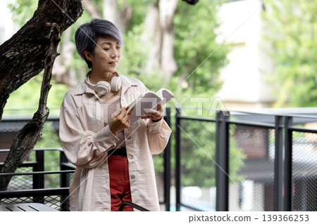 Asian adult woman enjoying peaceful reading time outdoors cafe balcony leisure activity promoting relaxation wellbeing lifestyle Asian adult woman enjoying peaceful reading time outdoors cafe balcony leisure activity promoting relaxation wellbeing lifestyle 139366253