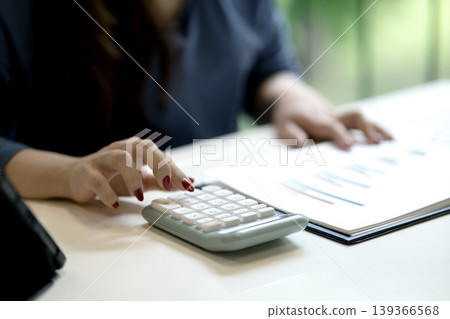 Business professional calculates financial figures analyzes data reviews market reports uses calculator office desk environment economic strategy planning Business professional calculates financial figures analyzes data reviews market reports uses calculator office desk environment economic strategy planning 139366568