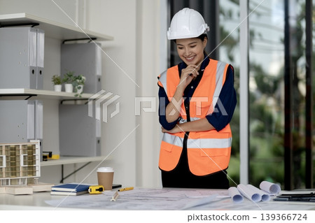 Adult Asian architect woman reviews building plans model at modern office site professional construction design development engineer smiles creating urban vision Adult Asian architect woman reviews building plans model at modern office site professional construction design development engineer smiles creating urban vision 139366724