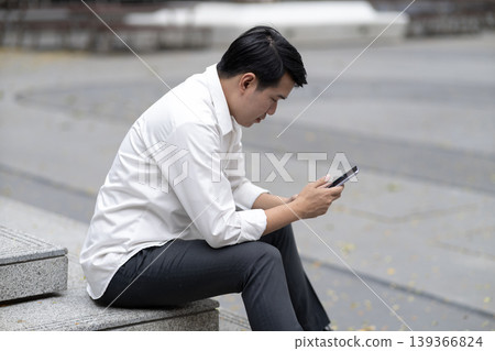 Asian adult man using smartphone outdoors focused communication technology business casual public space digital connection daily routine Asian adult man using smartphone outdoors focused communication technology business casual public space digital connection daily routine 139366824
