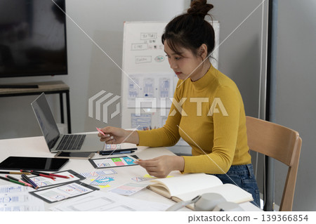 Asian woman designer creating modern user interface experience mobile application design using laptop tablet for digital product development research office workspace fostering creative innovation 139366854