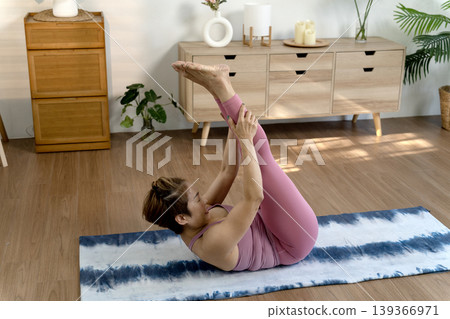 Adult Asian woman performs yoga core exercise stretching legs at home during morning fitness workout for healthy body wellness 139366971
