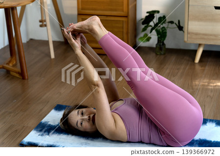 Asian adult woman practices yoga stretching at home for fitness health and wellness on wood floor during peaceful morning Asian adult woman practices yoga stretching at home for fitness health and wellness on wood floor during peaceful morning 139366972