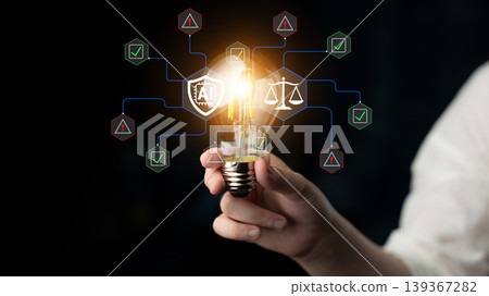 Hand Holding Light Bulb with Symbolic Illustrations of Innovation, Technology, Legal Concepts, and Data Protection in a Dark Background Fluxor Hand Holding Light Bulb with Symbolic Illustrations of Innovation, Technology, Legal Concepts, and Data Protection in a Dark Background Fluxor 139367282