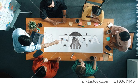 Aerial view of a team engaged in brainstorming during a meeting. The table features laptops, notes, and a creative illustration, highlighting active collaboration and innovation. Sigmoid Aerial view of a team engaged in brainstorming during a meeting. The table features laptops, notes, and a creative illustration, highlighting active collaboration and innovation. Sigmoid 139367449