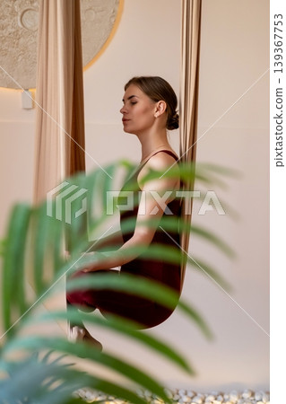 Mindfulness session. Retreat harmony. Calm woman sitting in fly yoga hammock in sport studio with green leaves. Zen atmosphere energy. Mindfulness session. Retreat harmony. Calm woman sitting in fly yoga hammock in sport studio with green leaves. Zen atmosphere energy. 139367753