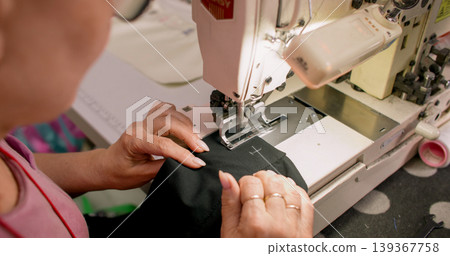 Clothing making. Sewing process. Tailor working on stitching professional machine. Woman creating buttonhole on black fabric sleeve. 139367758