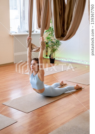 Bodyweight training. Physical therapy. Woman in sportswear pulling up with aerial yoga hammock doing flexibility exercise for muscle. 139367760