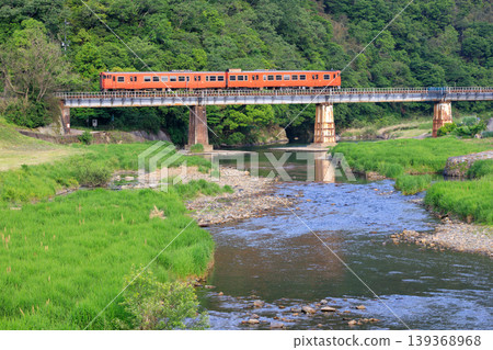 A reddish-brown diesel railcar of the Tsuyama Line crosses the Ukaigawa River on a clear May day. A reddish-brown diesel railcar of the Tsuyama Line crosses the Ukaigawa River on a clear May day. 139368968