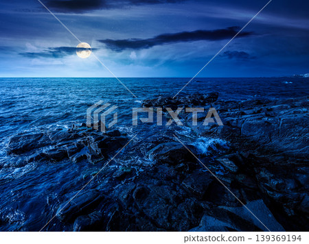 sea coast with stones and boulders at night. view of beach with rock in seaweed. full moon over dynamic cloudscape on the sky above horizon. mysterious summer vacations background concept sea coast with stones and boulders at night. view of beach with rock in seaweed. full moon over dynamic cloudscape on the sky above horizon. mysterious summer vacations background concept 139369194