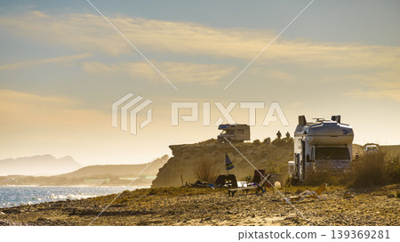 Camping by the water at a scenic location with two RVs parked near the shore during a sunny day Camping by the water at a scenic location with two RVs parked near the shore during a sunny day 139369281